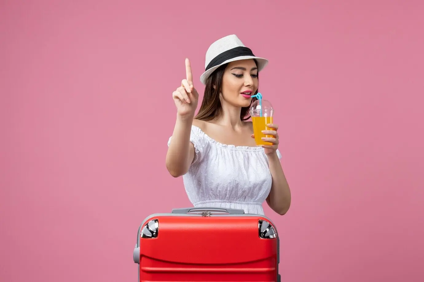 Vorderansicht einer jungen Frau, die im Sommerurlaub vor einer hellrosa Wand einen Cocktail hält; Ferien, Urlaubshitze, Reise, Sommertrip.